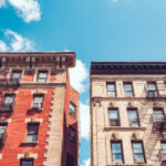 A view of two New York City apartment buildings side by side set against a blue sky
