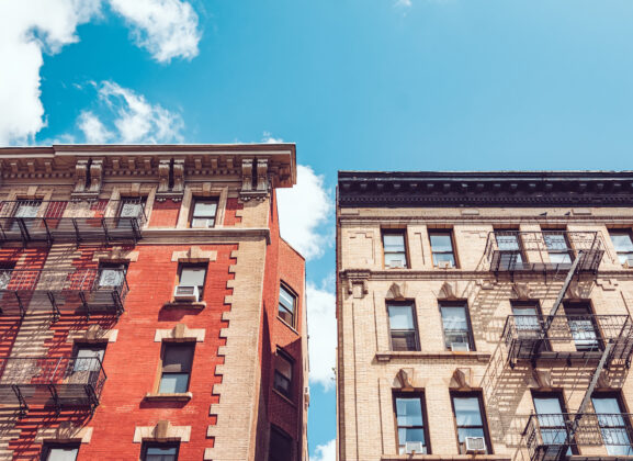 A view of two New York City apartment buildings side by side set against a blue sky