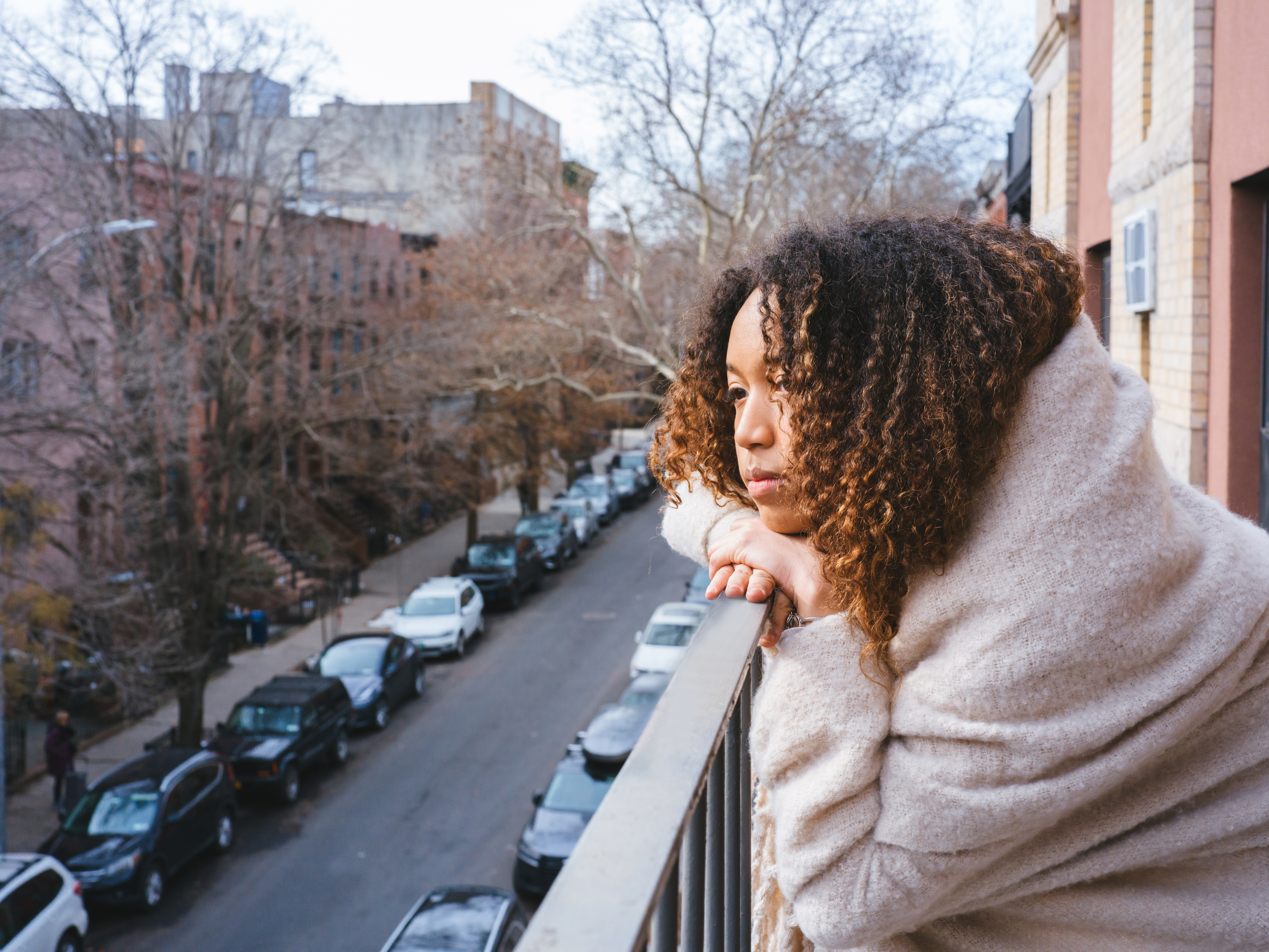 A young woman standing on her apartment balcony admiring the neighborhood view.