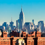 The New York City Skyline with the Empire State Building in the center of the frame rises above apartment buildings in the Lower East Side.