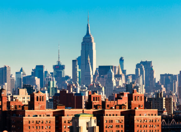 The New York City Skyline with the Empire State Building in the center of the frame rises above apartment buildings in the Lower East Side.