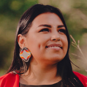 Portrait of Isabel Coronado. She has straight brown hair, festive earrings, and a red blazer.