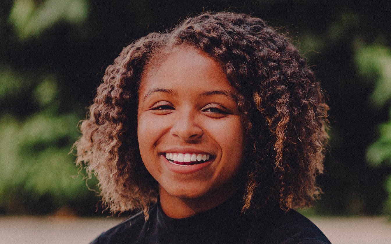 Portrait of Roquel Crutcher, she has a short curly hairstyle, a black shirt, and a wide smile.