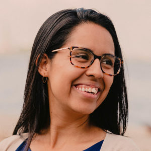 Portrait of Rosario Villarreal, she has straight black hair, tortoise shell glasses, and a wide smile.