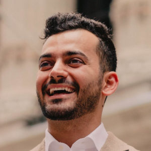 Portrait of Taif Jany. He has short, dark hair, a short beard and a wide smile.