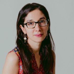 Portrait of Emma Vadehra. She has glasses, long dark hair, and gold dangly earings..