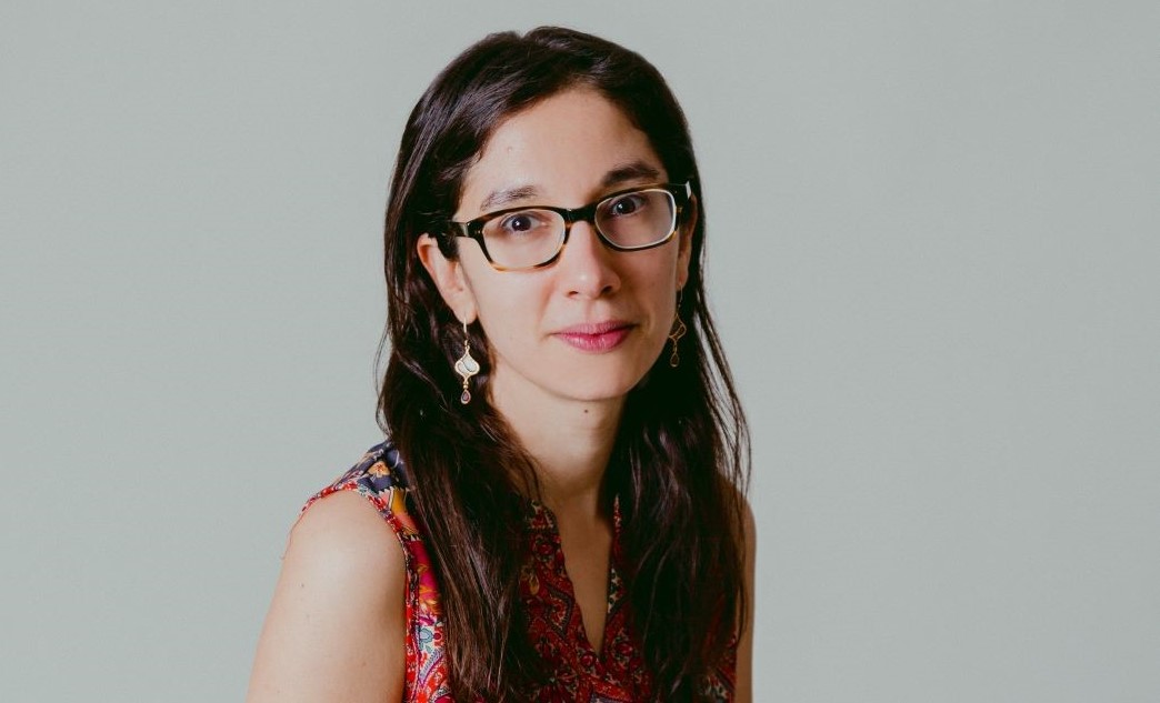 Portrait of Emma Vadehra. She has glasses, long dark hair, and gold dangly earings..